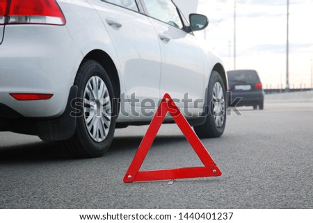 Road accident or 	vehicle breakdown  -  two cars white and black stopped on highway after collision. Red warning triangle in front of them, low angle shot Royalty-Free Stock Photo #1440401237