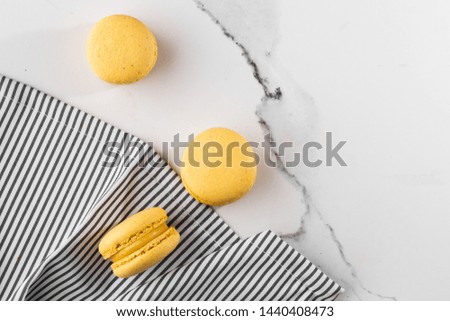 French macaroons isolated. Selective focus. Beautiful yellow macaroons in striped napkin on marble background. Stylish arrangement sweet. Flat lay, top view. Macro photo. With copy space.