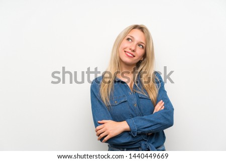 Young blonde woman over isolated white wall looking up while smiling