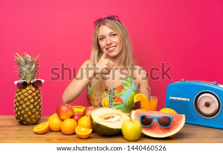 Young blonde woman with lots of fruits giving a thumbs up gesture
