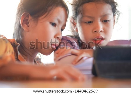 The older sister and sister are watching the cartoons on the mobile phone.