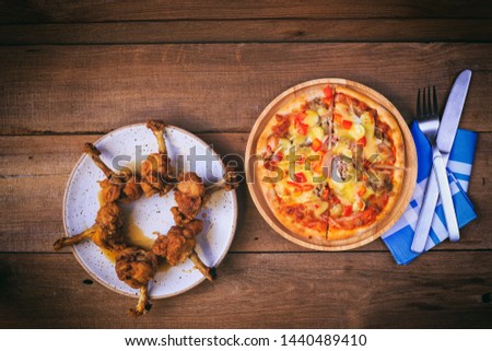 Vintage photography style of pizza and fried chicken, knife, fork, napkin on wooden table top, selected focus.