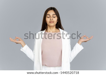 Calm healthy mindful indian business woman wear suit meditating doing yoga exercise with eyes closed breathing fresh air relaxing feel zen no stress free relief isolated on grey studio background