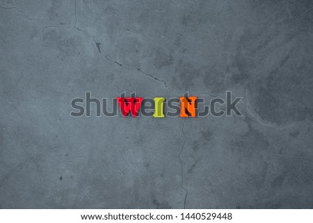 The multicolored win word is made of wooden letters on a grey plastered wall background.