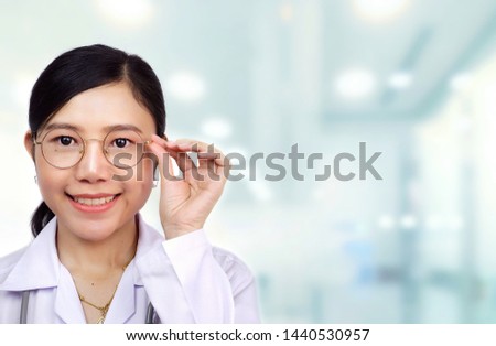 Beautiful young Asian female doctor with eyeglasses is smiling with blurred medical office background in occupation and medical healthcare concept, close up with copy space 