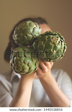 The girl holds three artichokes at head level with a blurred background, the concept of proper and dietary nutrition, dottex. horizontal picture