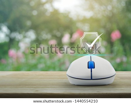 Security shield with check mark flat icon with wireless computer mouse on wooden table over blur pink flower and tree in park, Technology internet cyber security and anti virus concept