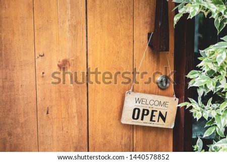 Wooden sign with text "Wecome we are open, please come in" hang on the vintage wooden front door of the cafe and restaurant.  Photography with copy space and background.