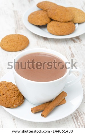 cup of cocoa with cinnamon and oatmeal cookies in the background, vertical