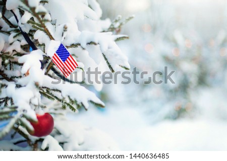 Christmas tree covered with snow and a flag of United States. American flag closeup. Winter background scene outdoor. Holiday greetings card