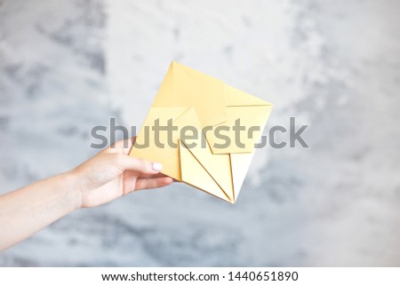 Female hand gives gold envelope square shape wedding invitation greeting card on gray background