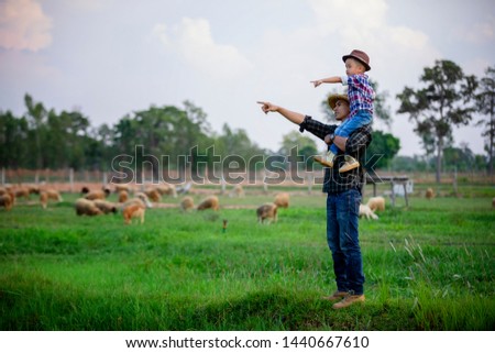 Father and son stood and watched the sheep on their farm and pointed their hands toward the sheep happily.
