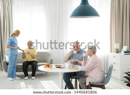 Nurse assisting elderly man while senior couple having breakfast at retirement home