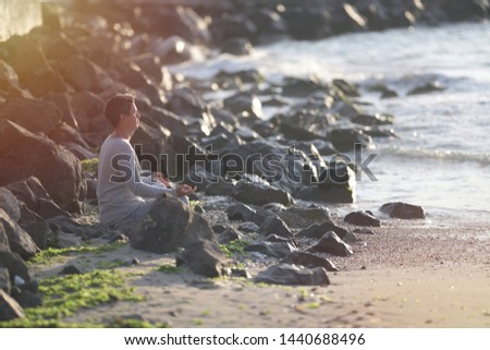 young man in meditation near the sea. Concept of pray. Adult practice yoga on the beach at sunset.