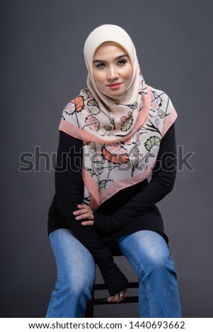 Beautiful female model wearing black color shirt and blue jeans with hijab, a modern lifestyle outfit  for Muslim woman isolated over grey background. Studio hijab fashion and beauty concept