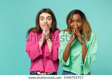Two young shocked surprised women friends european and african american in pink green clothes isolated on blue turquoise wall background, studio portrait. People lifestyle concept. Mock up copy space