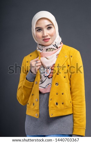 Fashionable female model in blue jeans, long sleeves yellow leather jacket with hijab isolated on grey background. Stylish Muslim female hijab fashion lifestyle portraiture concept.