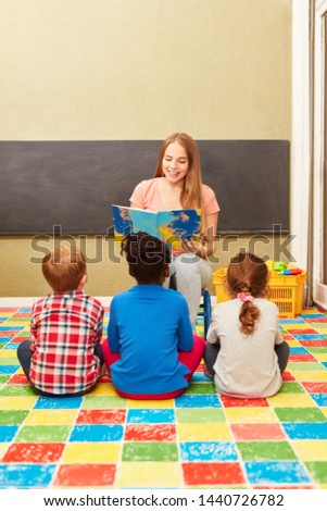 Woman as a kindergarten teacher and children reading from a children's book in kindergarten
