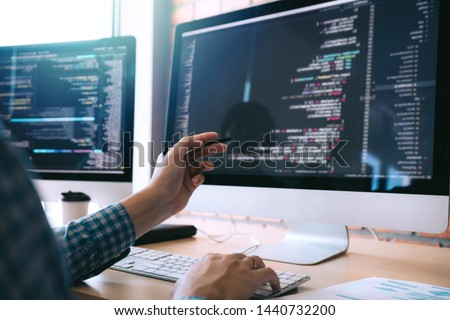 Software developer holds the pen pointing to the computer screen and is analyzing the code. Royalty-Free Stock Photo #1440732200