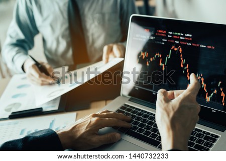 Investors are pointing to laptops that have investment information stock markets and partners taking notes and analyzing performance data. Royalty-Free Stock Photo #1440732233