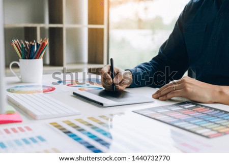 Freelance creative designers working on desk using digital graphic tablet and drawing with pen in modern home office.