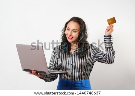 portrait of a joyful young woman holding a plastic Bank card and a laptop. Studio photo on white background