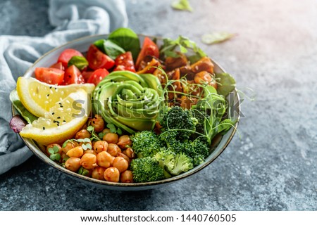 Buddha bowl salad with baked sweet potatoes, chickpeas, broccoli, tomatoes, greens, avocado, pea sprouts on light blue background with napkin. Healthy vegan food, clean eating, dieting, close up Royalty-Free Stock Photo #1440760505