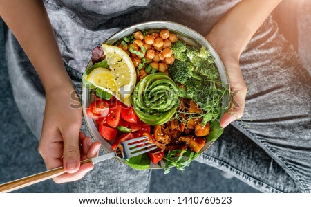 Woman in jeans holding Buddha bowl with salad, baked sweet potatoes, chickpeas, broccoli, greens, avocado, sprouts in hands. Healthy vegan food, clean eating, dieting, top view Royalty-Free Stock Photo #1440760523