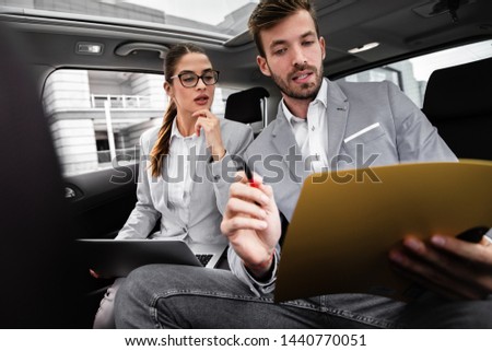 Young business people working together while traveling by a car. They are using laptop and preparing for meeting.	