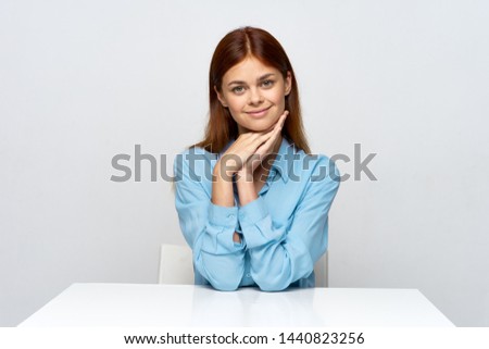 Blue shirt woman sitting at the table gray background hands near the face       
