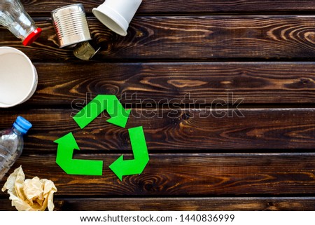 Recycling sign with waste materials, bottle, cups, can for ecology concept on wooden background top view mock up