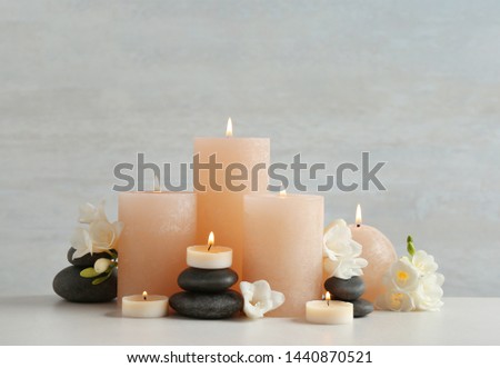 Beautiful composition with candles, stones and flowers on table against light background