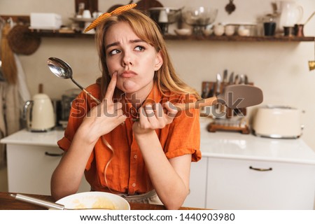 Picture of a confused sad young blonde girl chef cooking at the kitchen thinking.