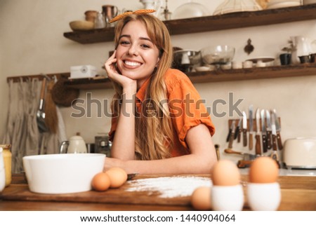 Picture of a cheery smiling young blonde girl chef cooking at the kitchen.