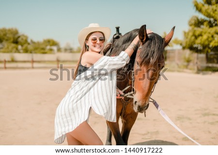 Girl in cowboy hat and shirt walking with a horse on a ranch