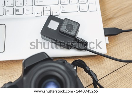 Action-camera connected to a laptop, on the background of a wooden table with a professional camera