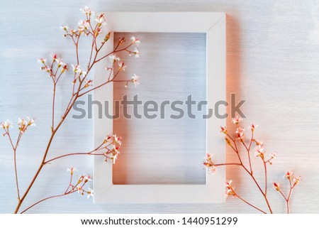 White wooden frame on a white textured background with small flowers - a template for a greeting card or invitation