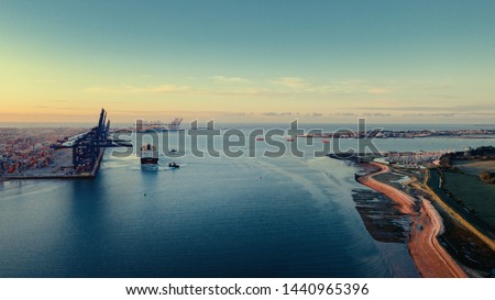 Sunrise over Felixstowe Container Port as two tugs help a container ship to cast off from the harbour wall and make it's way out to sea. Royalty-Free Stock Photo #1440965396