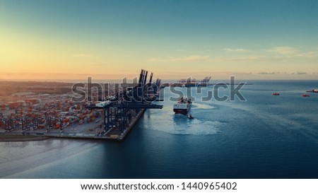 Sunrise over Felixstowe Container Port as two tugs help a container ship to cast off from the harbour wall and make it's way out to sea. Royalty-Free Stock Photo #1440965402