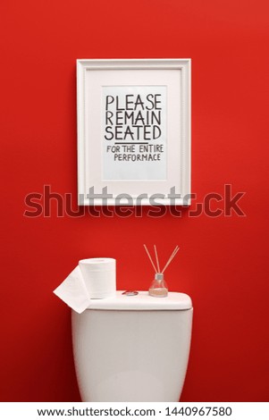 Toilet bowl and funny sign near red wall. Bathroom interior