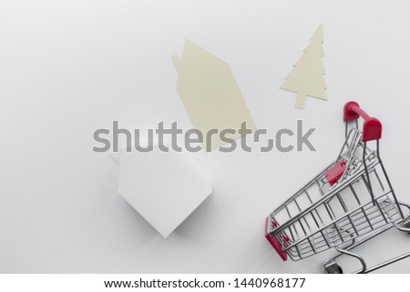 Paper cut out house and christmas tree with miniature house model and shopping cart isolated on white background