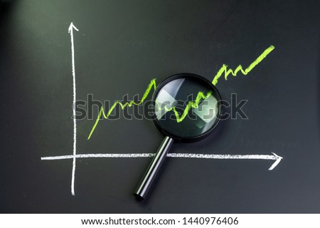 Black magnifying glass on chalk drawing green line stock or company performance graph and chart on blackboard using as financial analysis, profit and loss or searching for earning and yield. Royalty-Free Stock Photo #1440976406