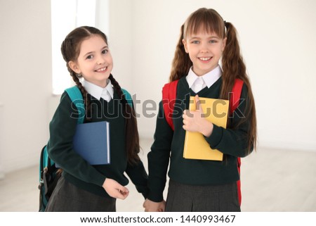 Portrait of cute girls in school uniform with backpacks and books indoors