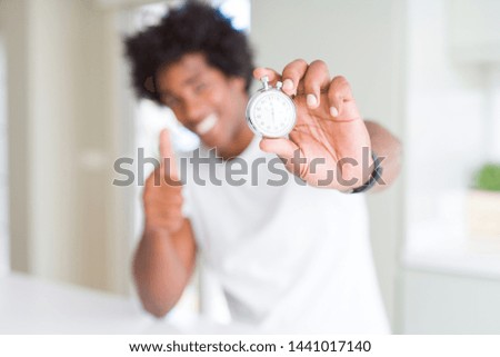 African American man holding stopwatch happy with big smile doing ok sign, thumb up with fingers, excellent sign