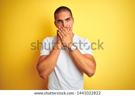 Young caucasian man wearing casual white t-shirt over yellow isolated background shocked covering mouth with hands for mistake. Secret concept.