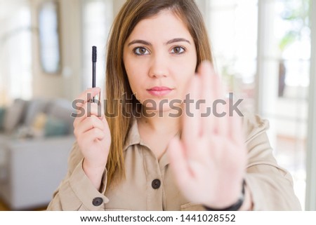 Beautiful young woman putting lash mascara on eyelashes with open hand doing stop sign with serious and confident expression, defense gesture