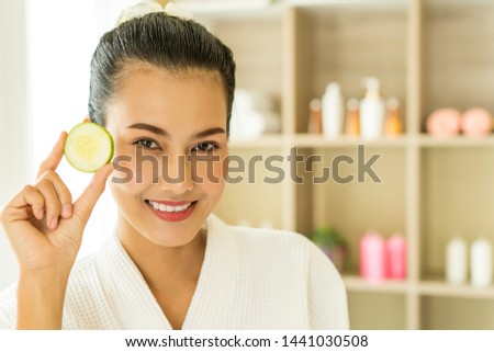 Portrait of charming young Asian women holding slices of fresh cucumber while relaxed from spa procedures on face with cucumber, covered with towel. spa,natural beauty, cosmetology and massage concept