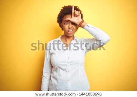 African american business woman over isolated yellow background making fun of people with fingers on forehead doing loser gesture mocking and insulting.