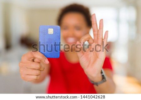 Young african american woman holding credit card doing ok sign with fingers, excellent symbol