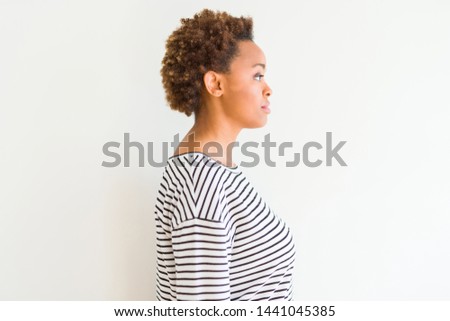 Young beautiful african american woman wearing stripes sweater over white background looking to side, relax profile pose with natural face with confident smile.
